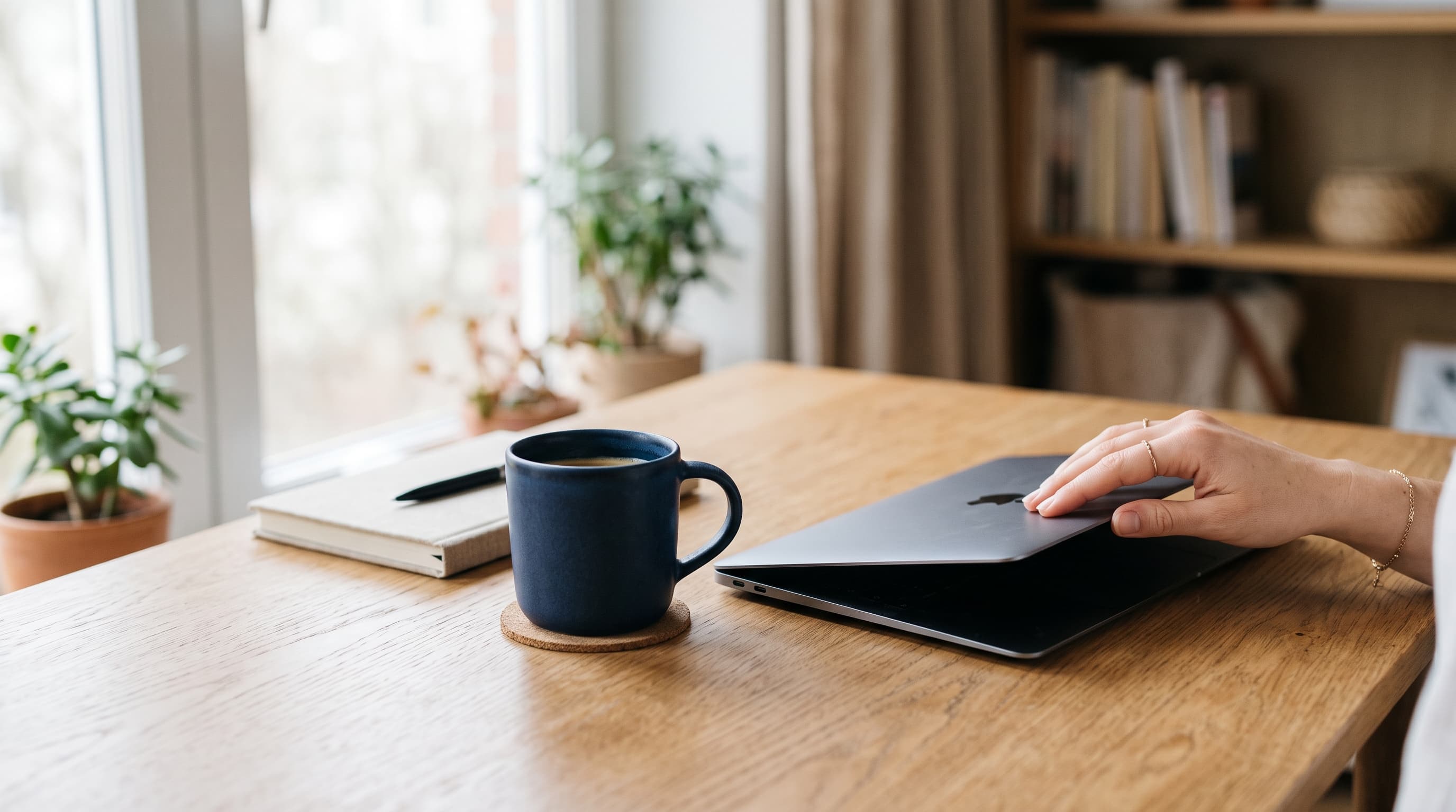 A calm, unhurried moment closing a laptop beside a ceramic mug on a clean desk